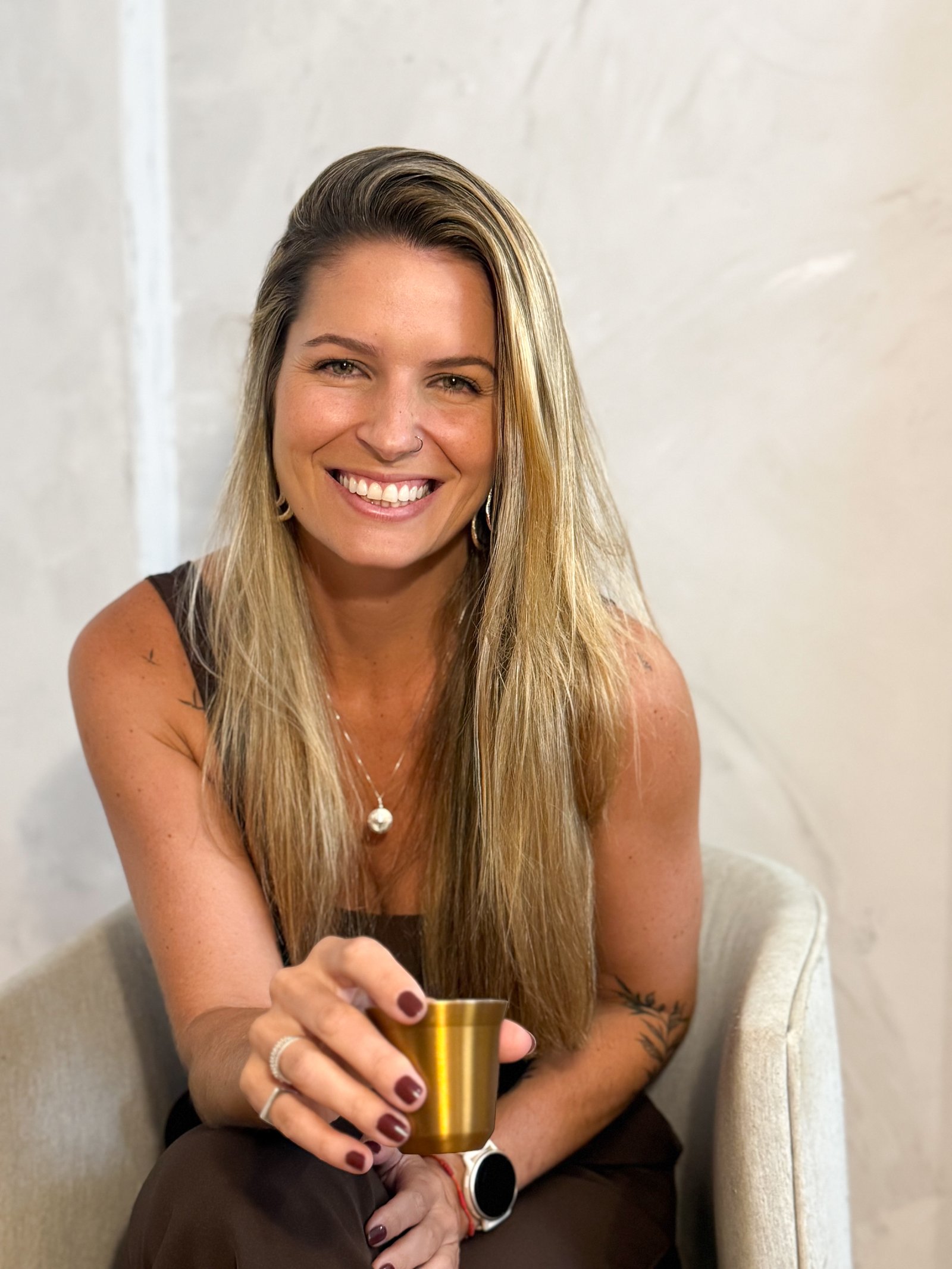 Juliana sorrindo, sentada numa poltrona, com uma xícara de café na mão